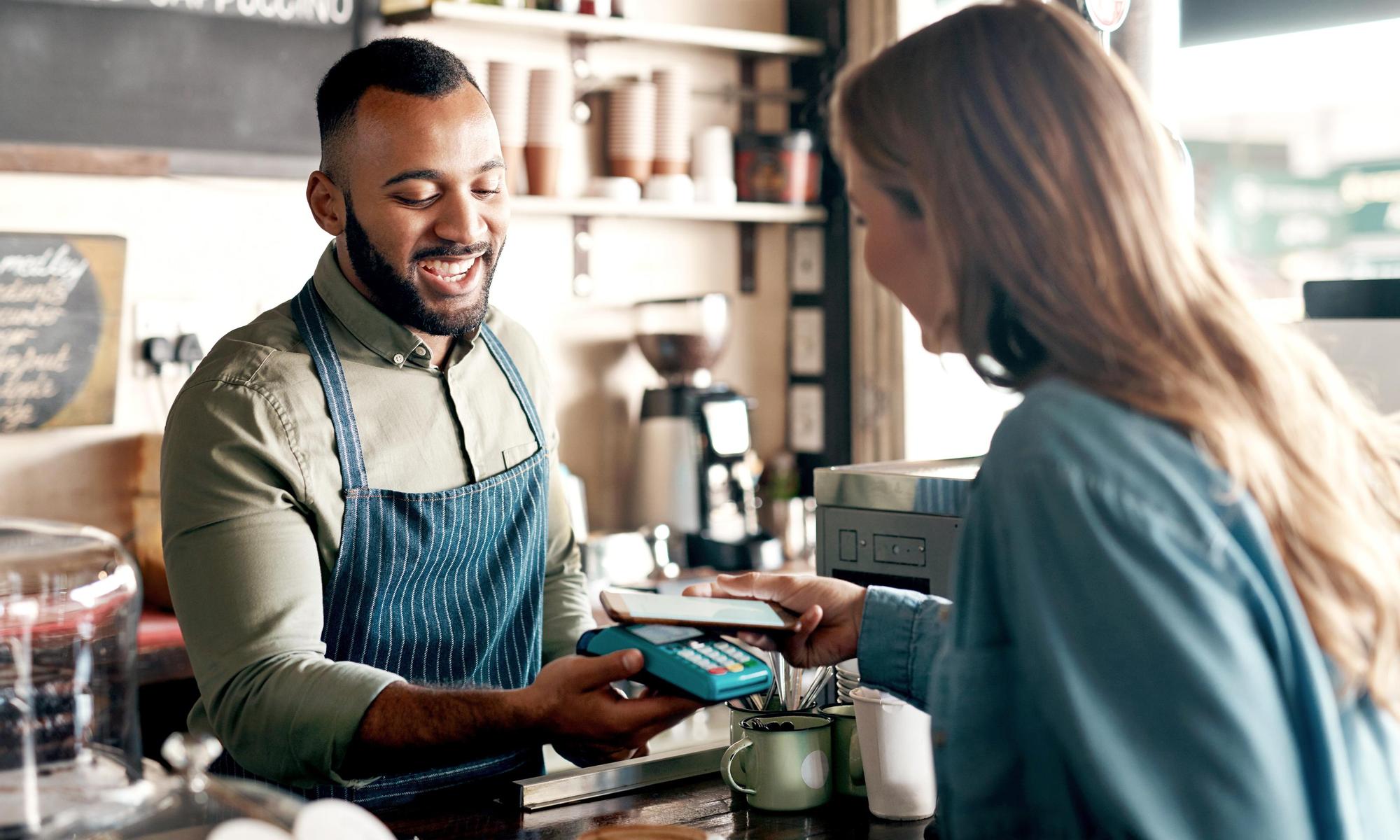 Young man accepting a digital payment from a customer in a cafe